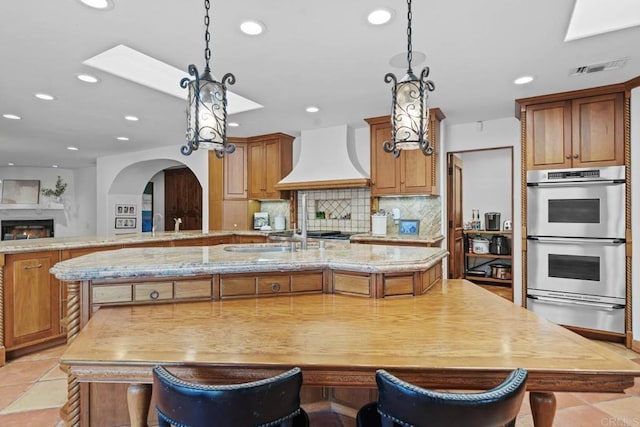 kitchen featuring a large island, stainless steel double oven, backsplash, a kitchen bar, and custom exhaust hood