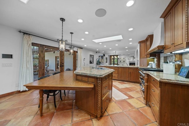 kitchen with a skylight, premium range hood, high end stainless steel range, hanging light fixtures, and an island with sink