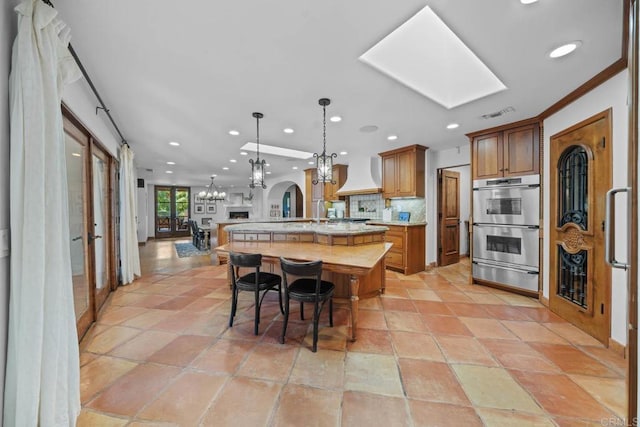 kitchen featuring decorative backsplash, ornamental molding, custom exhaust hood, double oven, and hanging light fixtures