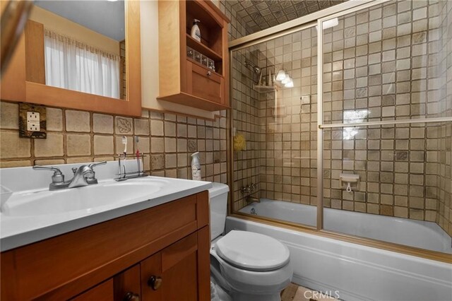 full bathroom with combined bath / shower with glass door, backsplash, vanity, tile walls, and toilet