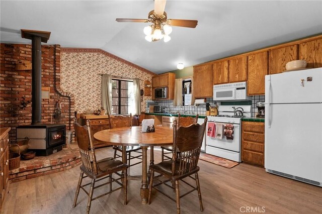 kitchen with light wood-type flooring, white appliances, ceiling fan, a wood stove, and lofted ceiling