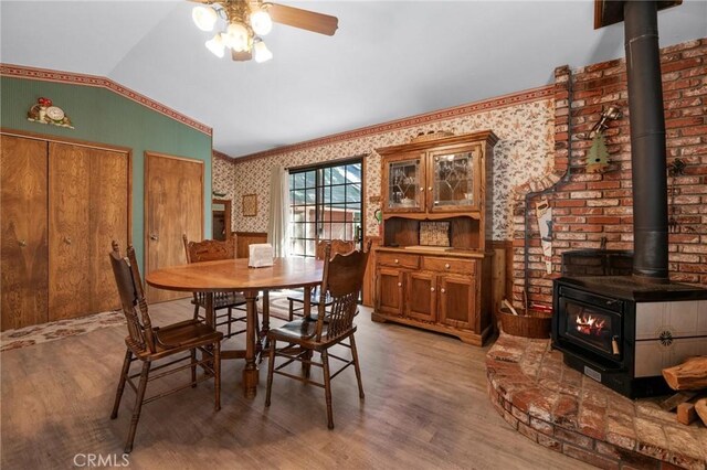 dining space with a wood stove, hardwood / wood-style flooring, vaulted ceiling, and ceiling fan