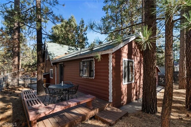 view of home's exterior featuring a deck, outdoor dining area, log veneer siding, and fence