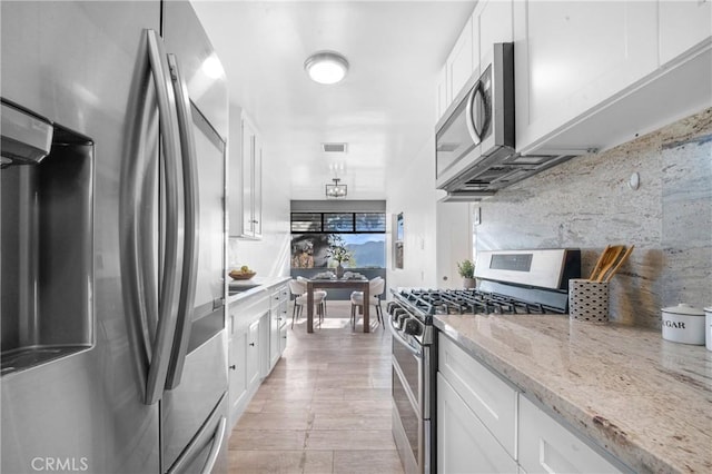 kitchen with appliances with stainless steel finishes, tasteful backsplash, light stone counters, white cabinets, and light hardwood / wood-style floors