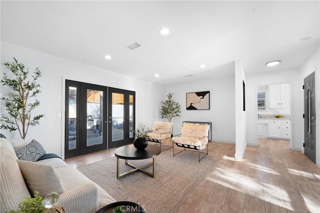 living room with decorative columns, light wood-type flooring, and french doors