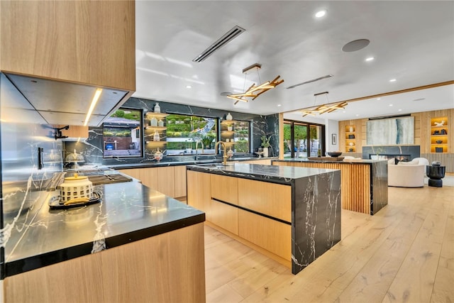 kitchen with dark stone counters, light brown cabinetry, a spacious island, and light hardwood / wood-style floors