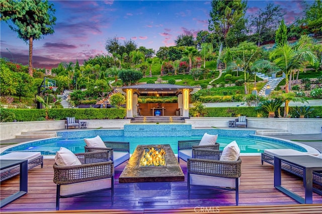 pool at dusk with a fire pit, a gazebo, and a wooden deck