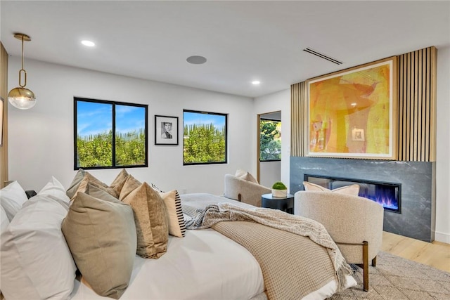 bedroom featuring multiple windows, a premium fireplace, and light hardwood / wood-style floors