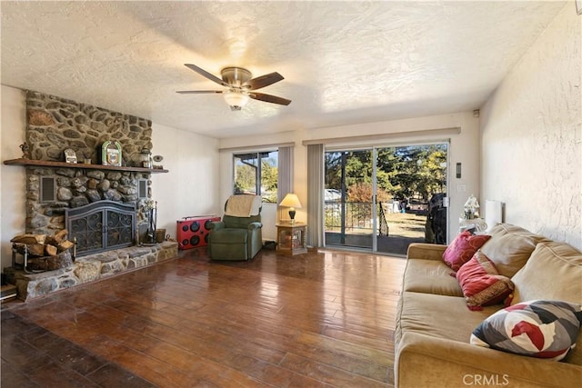 living room featuring hardwood / wood-style flooring, ceiling fan, a stone fireplace, and a textured ceiling