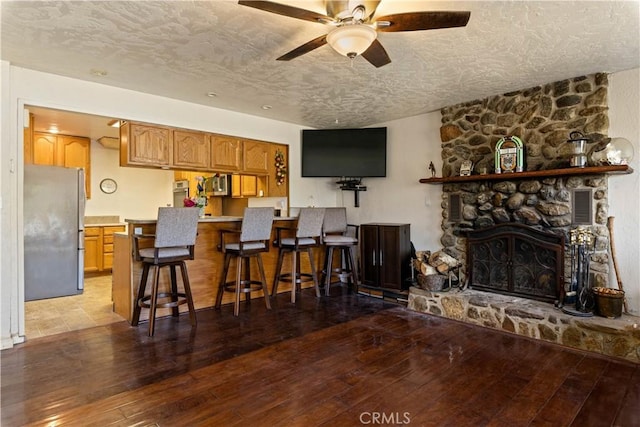 kitchen with a kitchen bar, a textured ceiling, stainless steel appliances, light hardwood / wood-style floors, and a stone fireplace