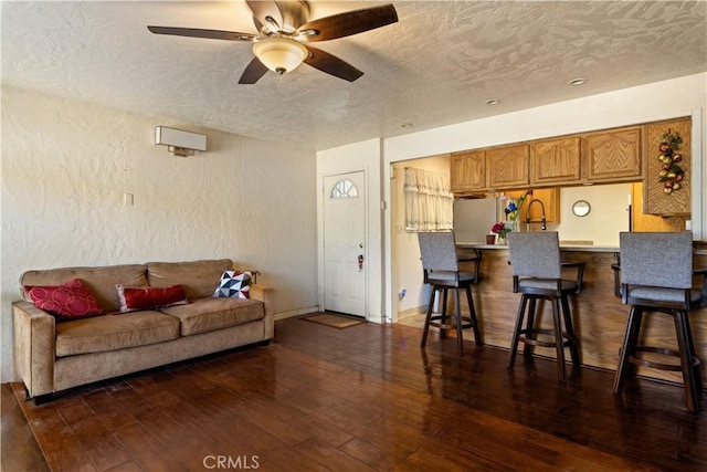 living room with a textured ceiling, ceiling fan, and dark wood-type flooring