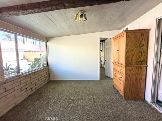 spare room featuring lofted ceiling with beams, wooden ceiling, brick wall, and dark carpet