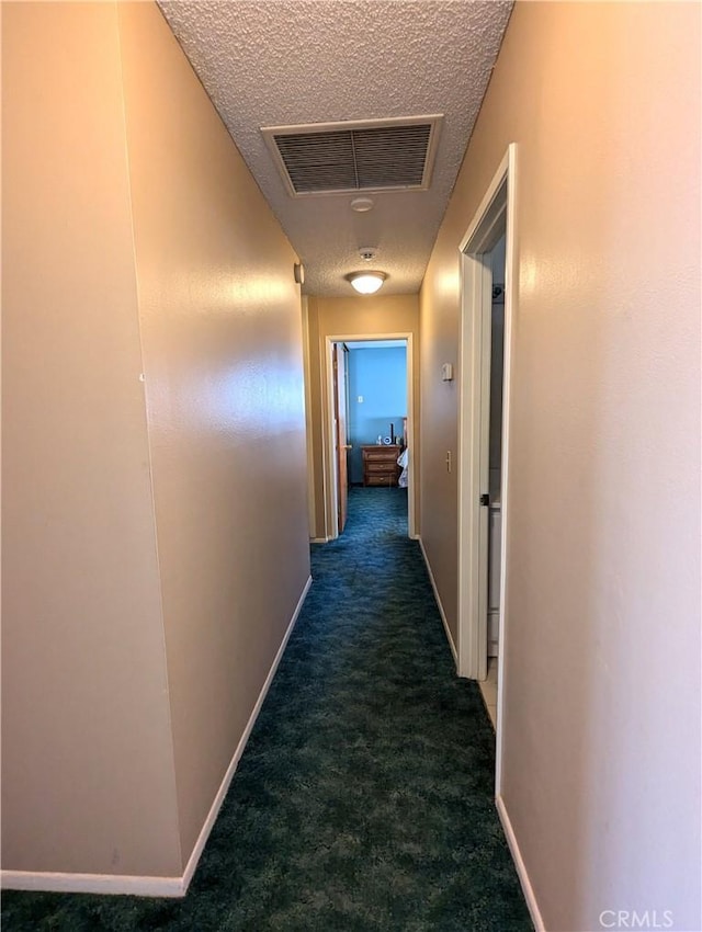 hallway featuring dark carpet and a textured ceiling