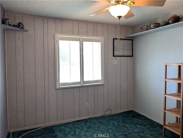 empty room featuring dark carpet, a textured ceiling, and wooden walls