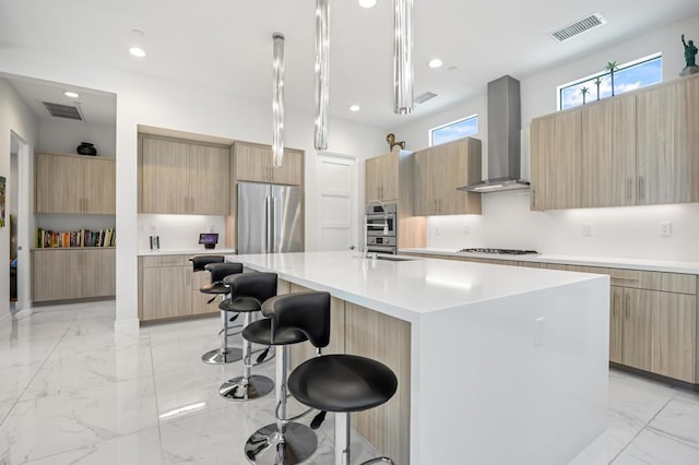 kitchen with pendant lighting, wall chimney exhaust hood, an island with sink, a kitchen bar, and stainless steel appliances