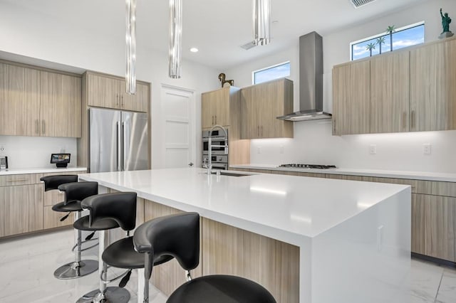 kitchen featuring a large island with sink, appliances with stainless steel finishes, hanging light fixtures, and wall chimney exhaust hood