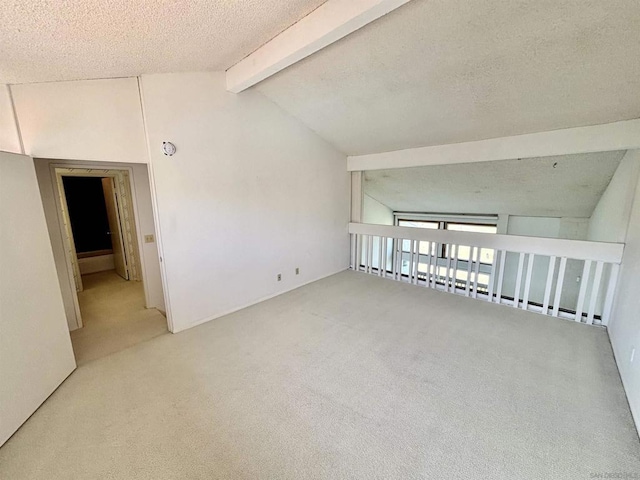 unfurnished room featuring a textured ceiling, vaulted ceiling with beams, and light carpet