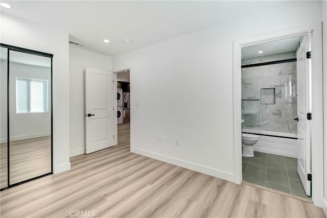 bedroom with light wood-type flooring, a closet, independent washer and dryer, and ensuite bath