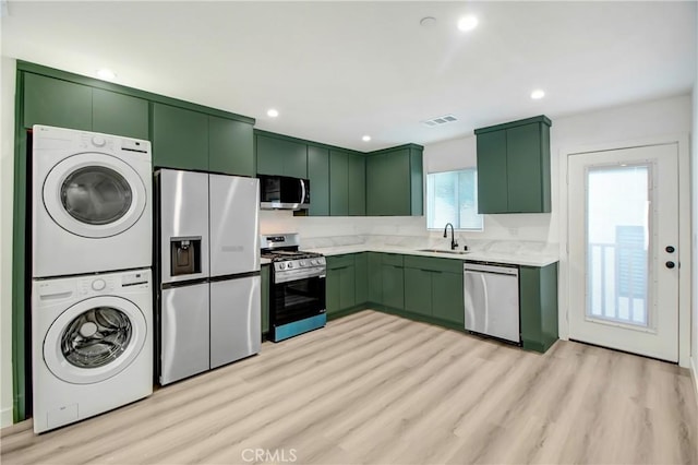 kitchen featuring stainless steel appliances, light hardwood / wood-style floors, sink, stacked washer and clothes dryer, and green cabinets