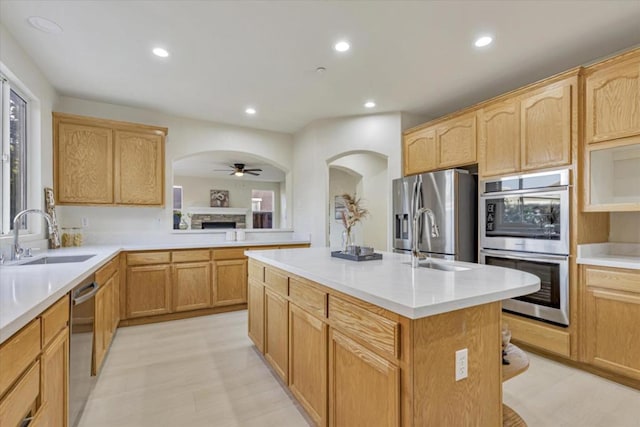 kitchen featuring appliances with stainless steel finishes, ceiling fan, a kitchen island with sink, sink, and a fireplace