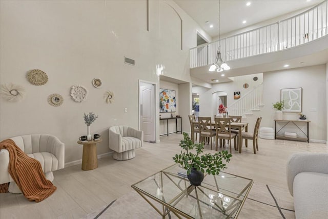 living room featuring an inviting chandelier, a towering ceiling, and light hardwood / wood-style flooring