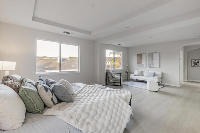 bedroom with light hardwood / wood-style floors and a tray ceiling