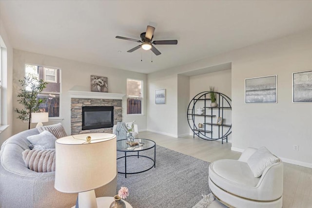 living room with a stone fireplace, ceiling fan, and light wood-type flooring