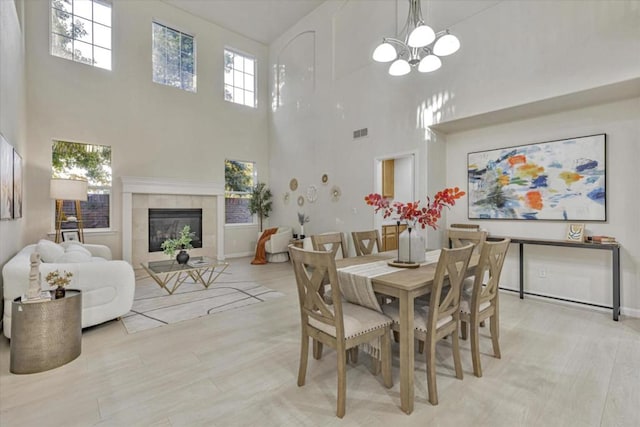 dining area with a notable chandelier, a towering ceiling, light hardwood / wood-style flooring, and a tiled fireplace