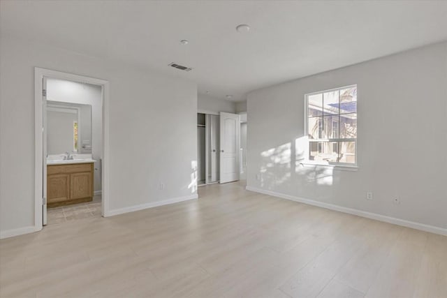 unfurnished bedroom with ensuite bath and light wood-type flooring