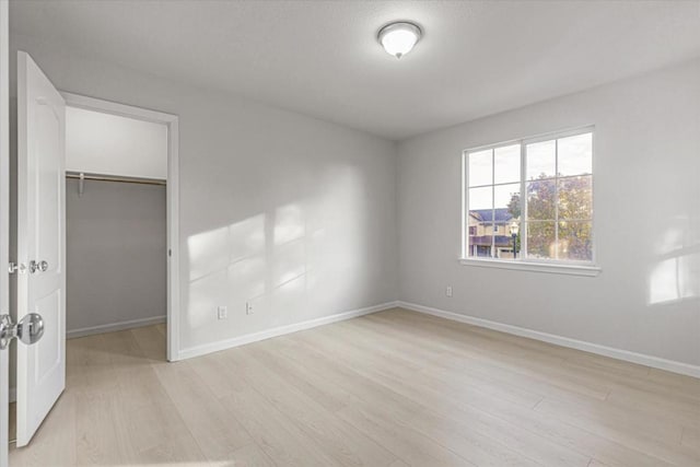 unfurnished bedroom featuring a walk in closet, a closet, and light hardwood / wood-style flooring