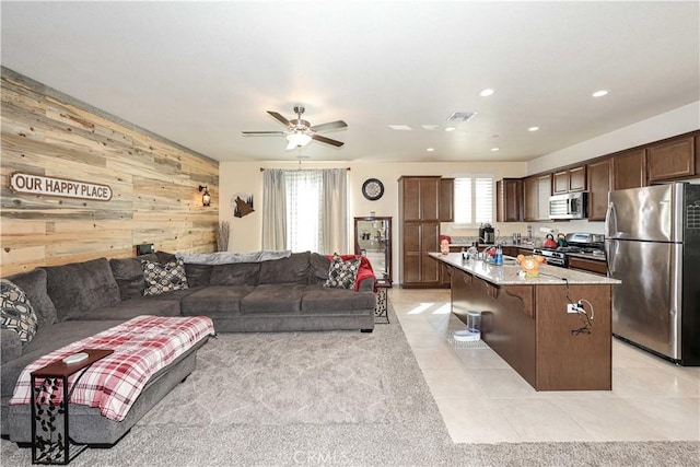 living room with light tile patterned floors, ceiling fan, and wooden walls