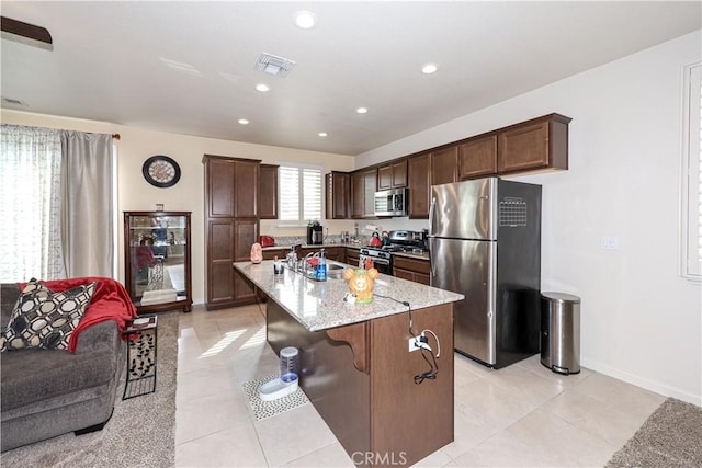 kitchen with dark brown cabinetry, light stone countertops, stainless steel appliances, a breakfast bar area, and a kitchen island with sink