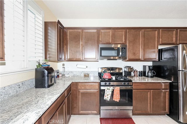 kitchen with appliances with stainless steel finishes, light tile patterned floors, and light stone counters