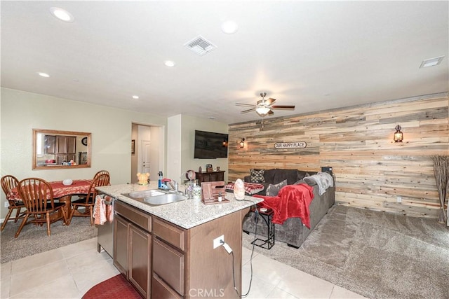 kitchen featuring ceiling fan, sink, wood walls, light colored carpet, and a kitchen island with sink