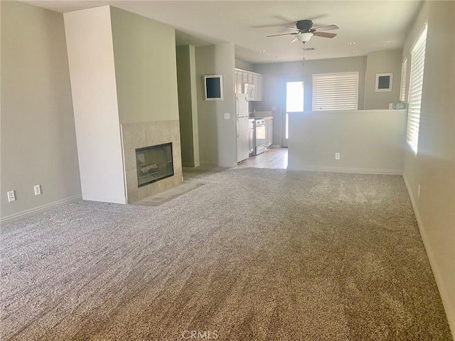 unfurnished living room featuring ceiling fan, light colored carpet, and a tiled fireplace