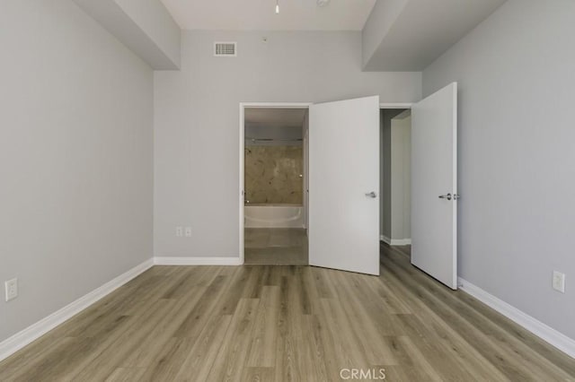 unfurnished bedroom featuring ensuite bathroom and light wood-type flooring