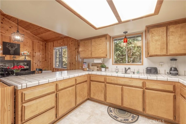 kitchen featuring tile counters, plenty of natural light, wood walls, and lofted ceiling