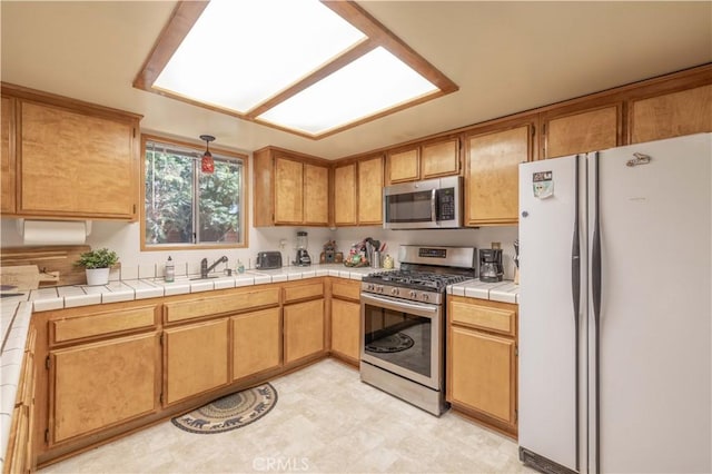 kitchen with tile countertops, sink, and appliances with stainless steel finishes