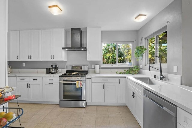 kitchen featuring white cabinets, wall chimney range hood, sink, light tile patterned floors, and stainless steel appliances