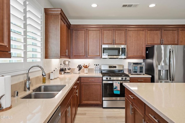 kitchen with light stone countertops, stainless steel appliances, light hardwood / wood-style flooring, and sink