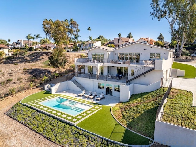 back of house with a lawn, a patio area, an in ground hot tub, and a balcony