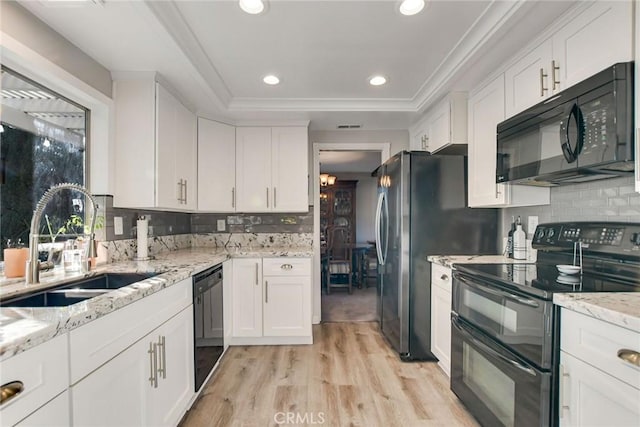 kitchen with light wood-type flooring, backsplash, sink, black appliances, and white cabinetry