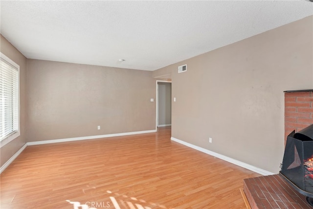 unfurnished living room featuring a wood stove, a textured ceiling, and light hardwood / wood-style flooring