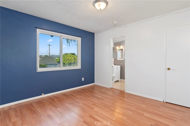 unfurnished bedroom featuring a textured ceiling, light hardwood / wood-style flooring, and ensuite bath