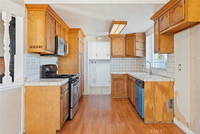 kitchen with sink, appliances with stainless steel finishes, tasteful backsplash, tile counters, and light hardwood / wood-style floors