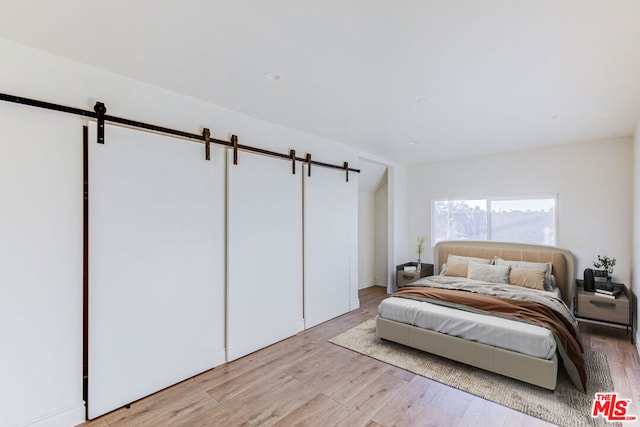 bedroom featuring a barn door and light hardwood / wood-style floors