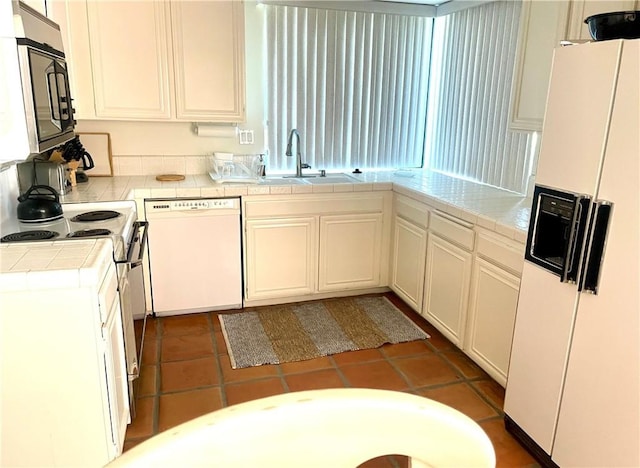 kitchen featuring white appliances, white cabinets, sink, dark tile patterned floors, and tile counters