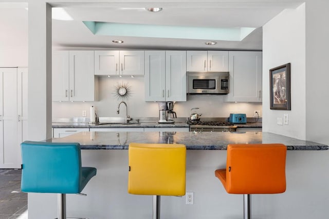 kitchen featuring white cabinetry, sink, kitchen peninsula, a kitchen bar, and appliances with stainless steel finishes