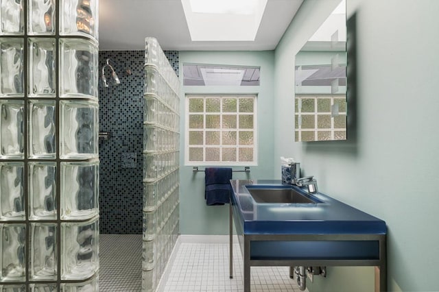 bathroom with tile patterned flooring, tiled shower, sink, and a skylight