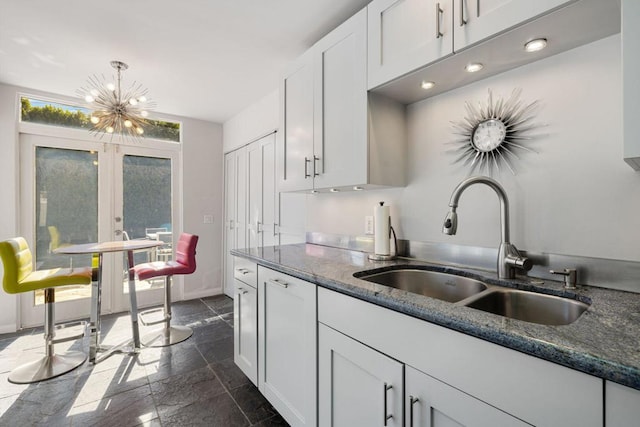 kitchen featuring dark stone counters, sink, decorative light fixtures, an inviting chandelier, and white cabinetry